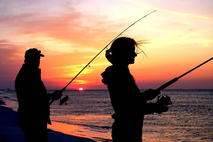 Two people fishing on the Emerald Isle beach at sunrise.