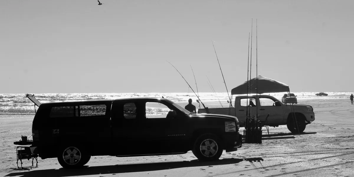 Black and white photo of several trucks and fishing rods on the beach.